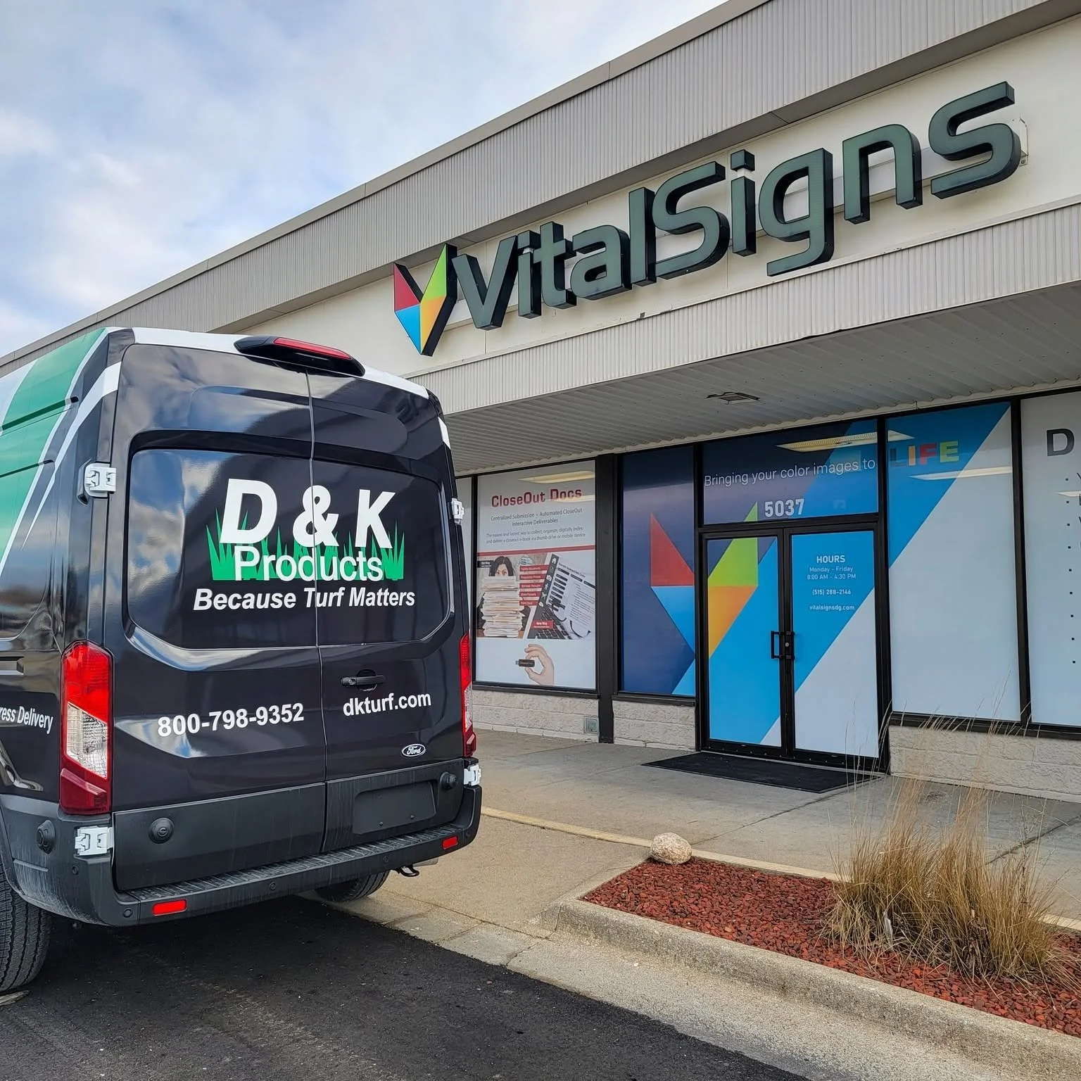 Storefront of VitalSigns business with a parking lot in front. A service van from D&K Products is parked outside, with branding and contact information visible.