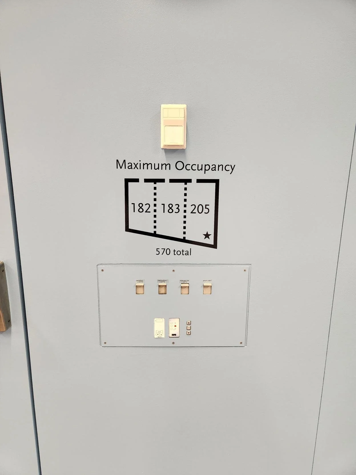 Building directory panel with maximum occupancy sign, showing three rooms numbered 182, 183, and 205, with a total of 570 occupants allowed.