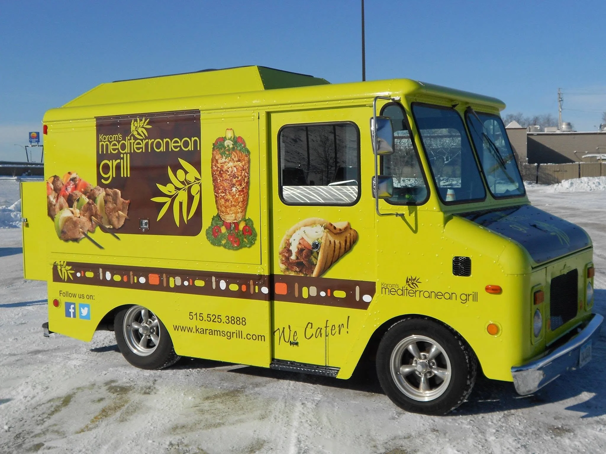 Bright yellow food truck with advertising for Mediterranean grill, featuring images of kebabs, a wrap, and grilled meat, parked in a snowy area with a clear blue sky.