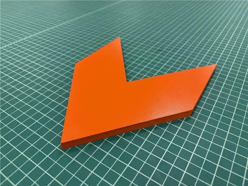 Orange downward arrow-shaped sign on green cutting mat.