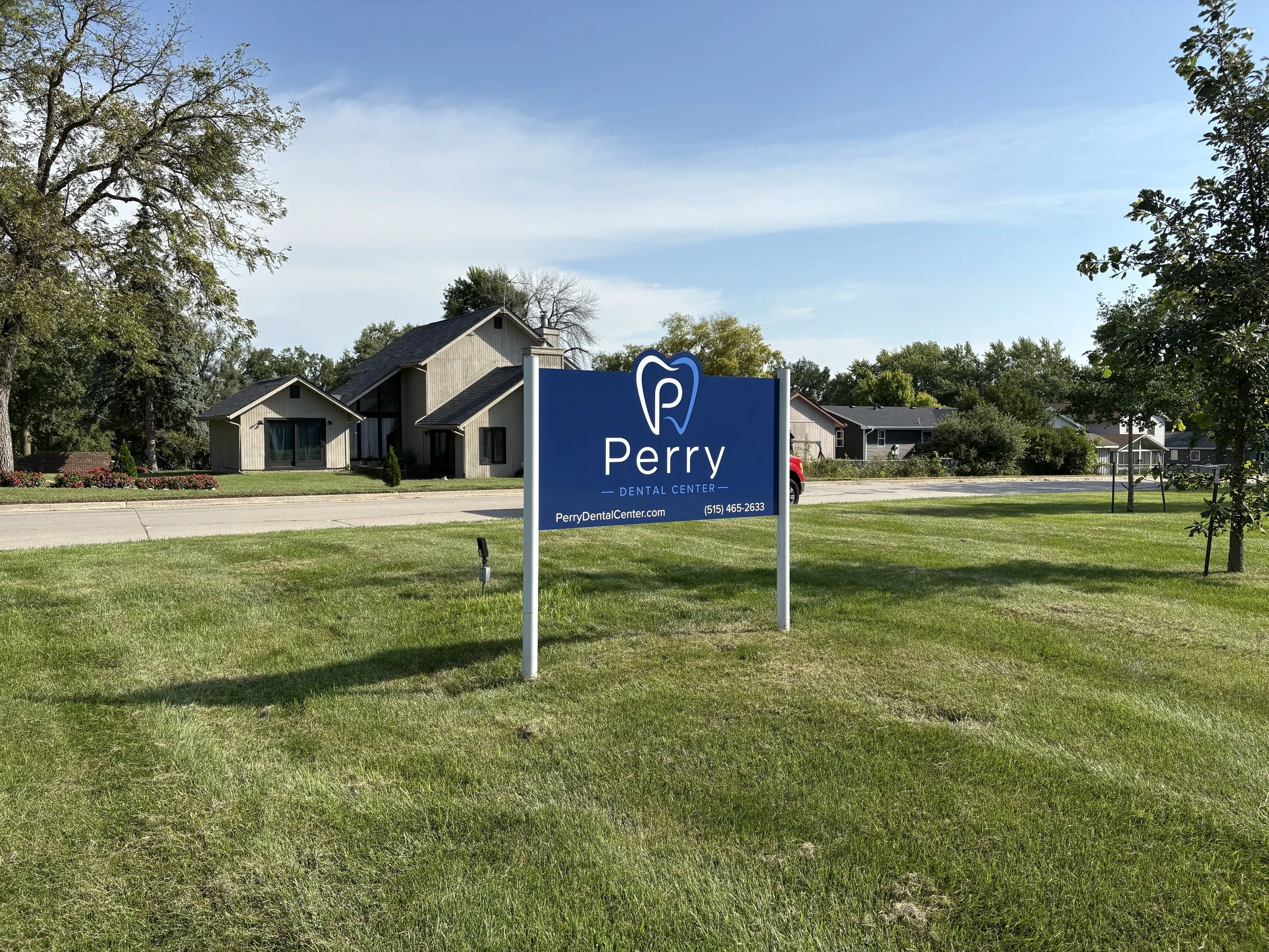 A cityscape with houses, trees, and a blue sky with some clouds. A sign for Perry Dental Center is in the foreground.