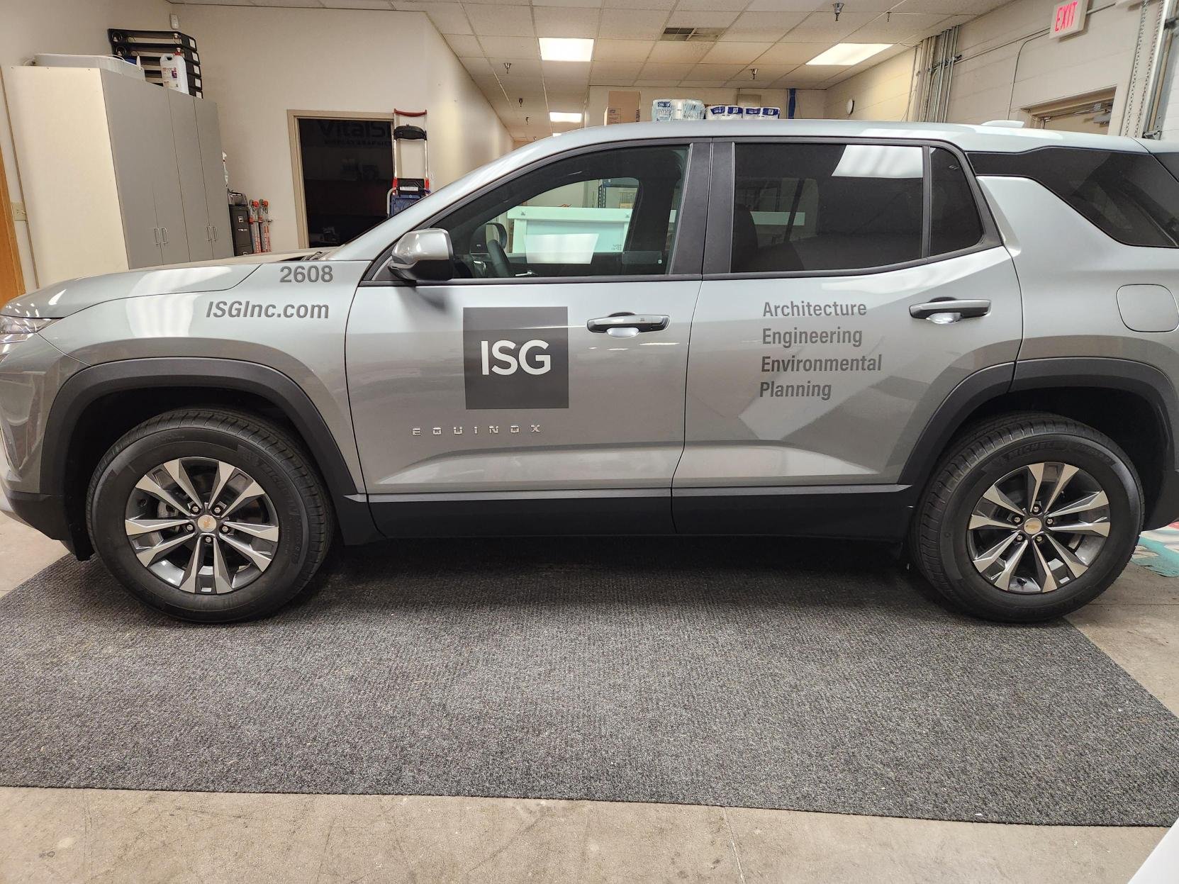Silver SUV parked indoors with ISG branding and company information on the side, including website, phone number, and services related to architecture, engineering, environmental, and planning.