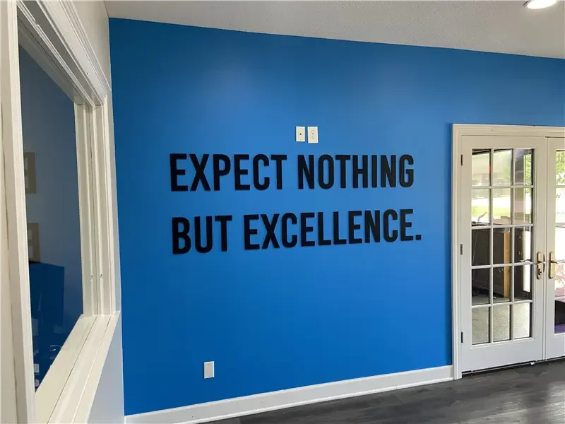 Blue wall with black dimensional acrylic letters saying "EXPECT NOTHING BUT EXCELLENCE." in a room with a window and a set of French doors.
