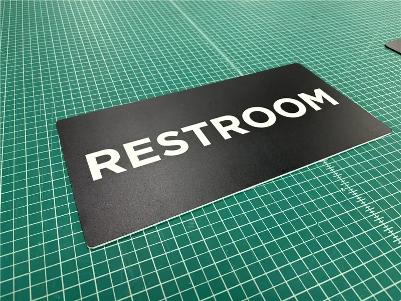 Black restroom sign with white text on a green cutting mat