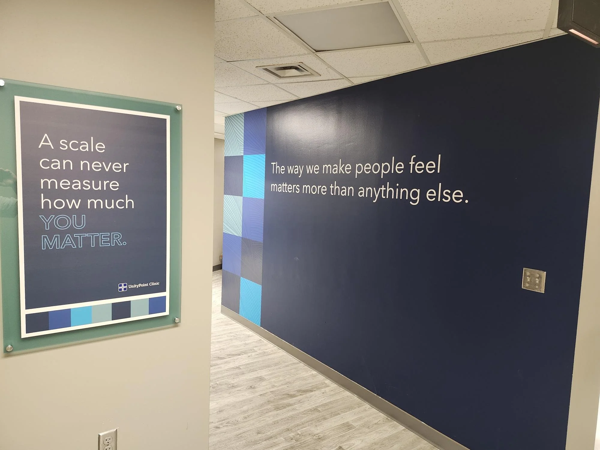 Interior of a medical or clinic office with blue walls and signs displaying motivational quotes about the importance of feeling and caring, including phrases like 'A scale can never measure how much you matter' and 'The way we make people feel matter