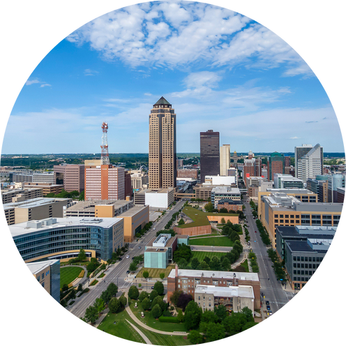 A city skyline with tall buildings, a mix of modern and older architecture, and green parks in an urban area under a partly cloudy blue sky.