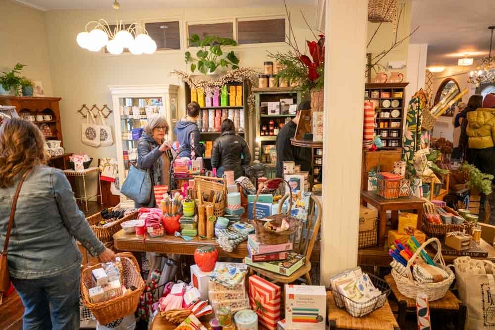 Inside a boutique store with shelves and tables filled with colorful gift items, decorations, and wrapped packages. Customers browse and shop.