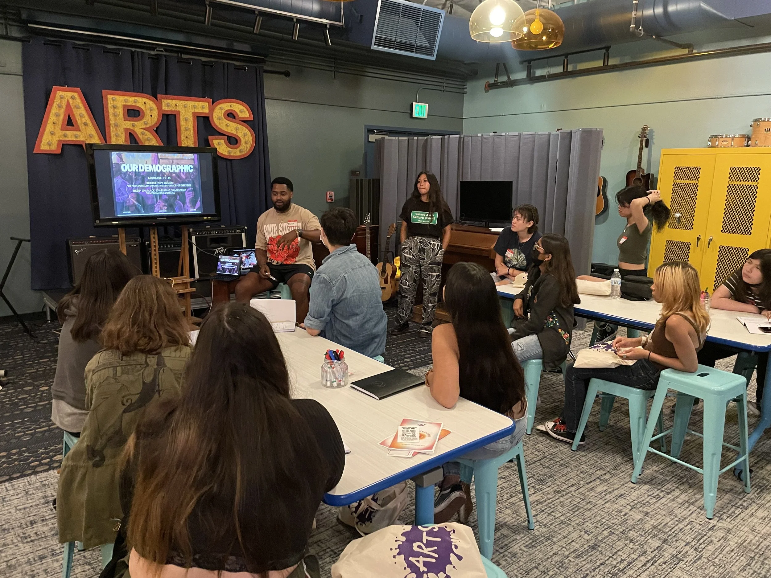 A workshop in the ARTS music room hosted by Sound Future. Blake Dye (SMPL Collective, Soul Sunday) and Lauren Garces (Social Artistry) face a room full of attentive listeners as ton Event Planning. The two are facing a room of young people listening