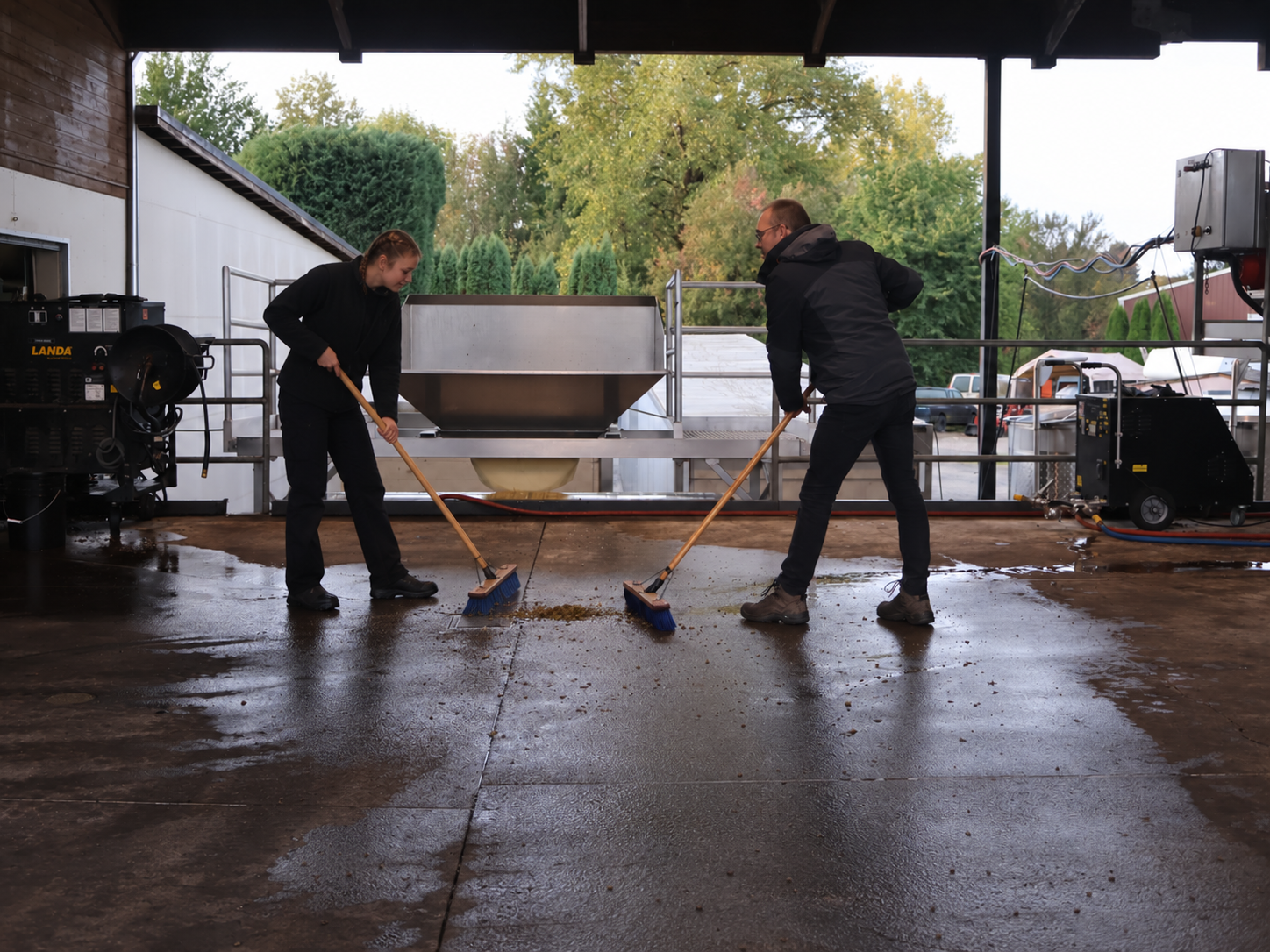 Two winemakers sweep the crush pad after pressing