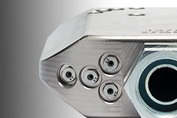 Close-up of a metallic silver device with four circular ports or sensors on its side.