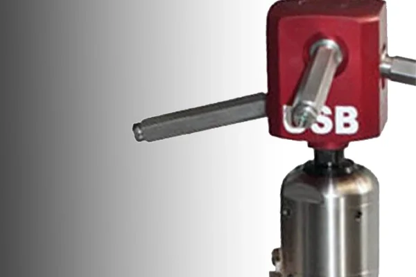 Close-up of a metal laboratory or industrial instrument with a red component marked 'SB,' a horizontal arm, and a shiny cylindrical base.