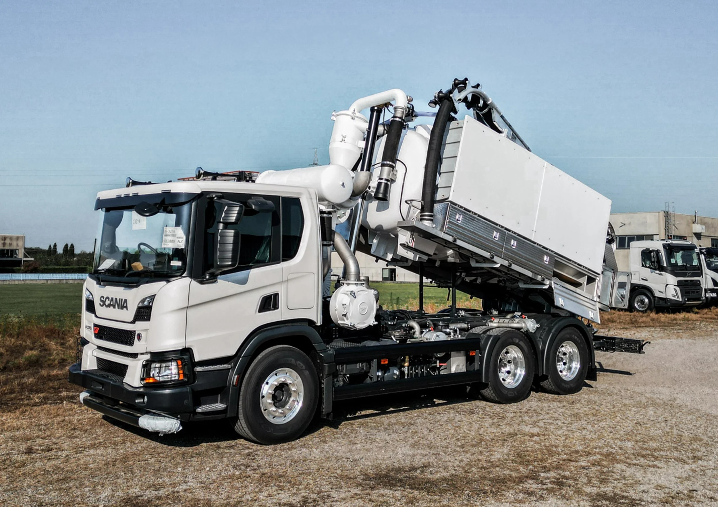 A large white mobile crane truck parked on a grassy field with a clear blue sky in the background.