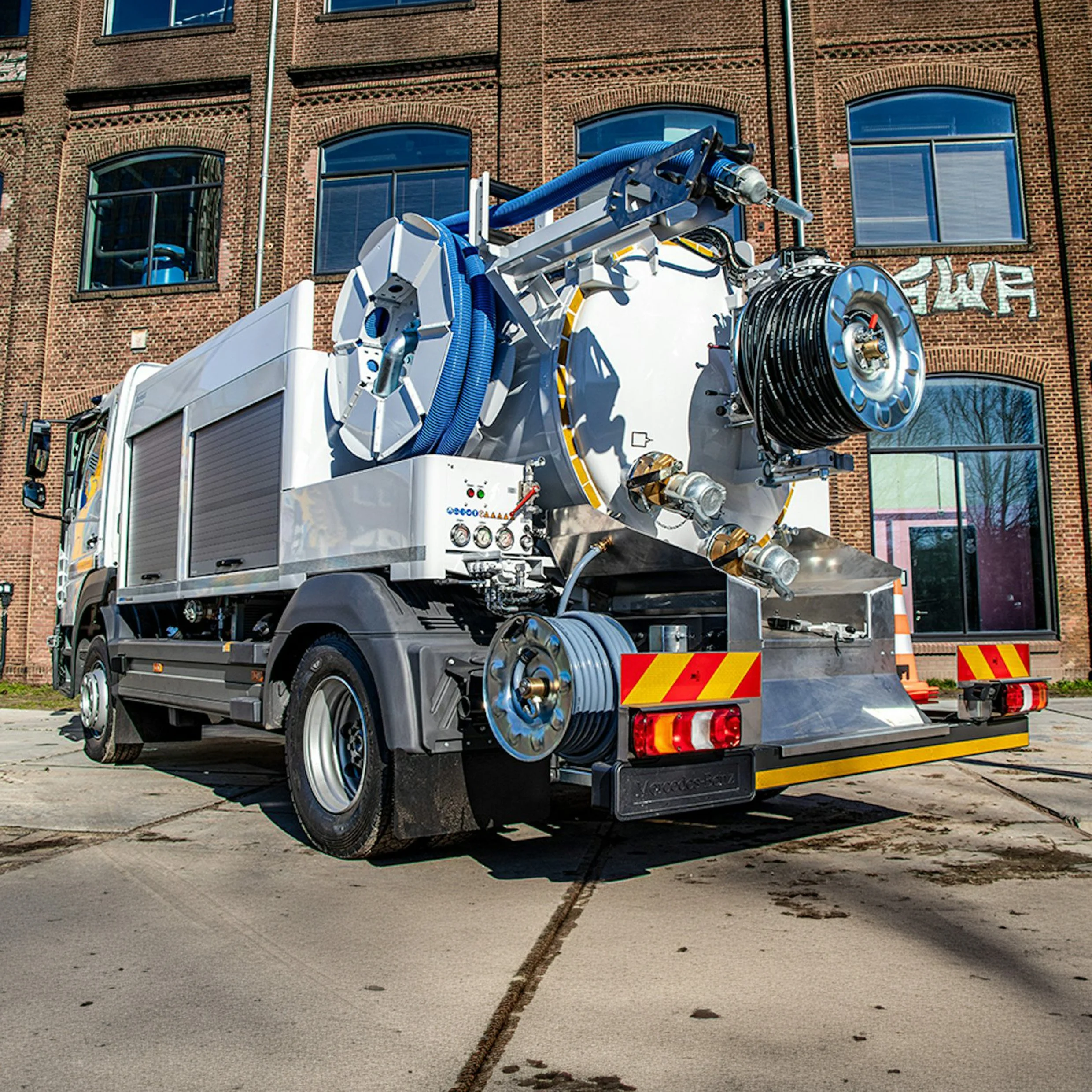 A fire truck with firefighting equipment parked in front of a brick building with multiple windows.