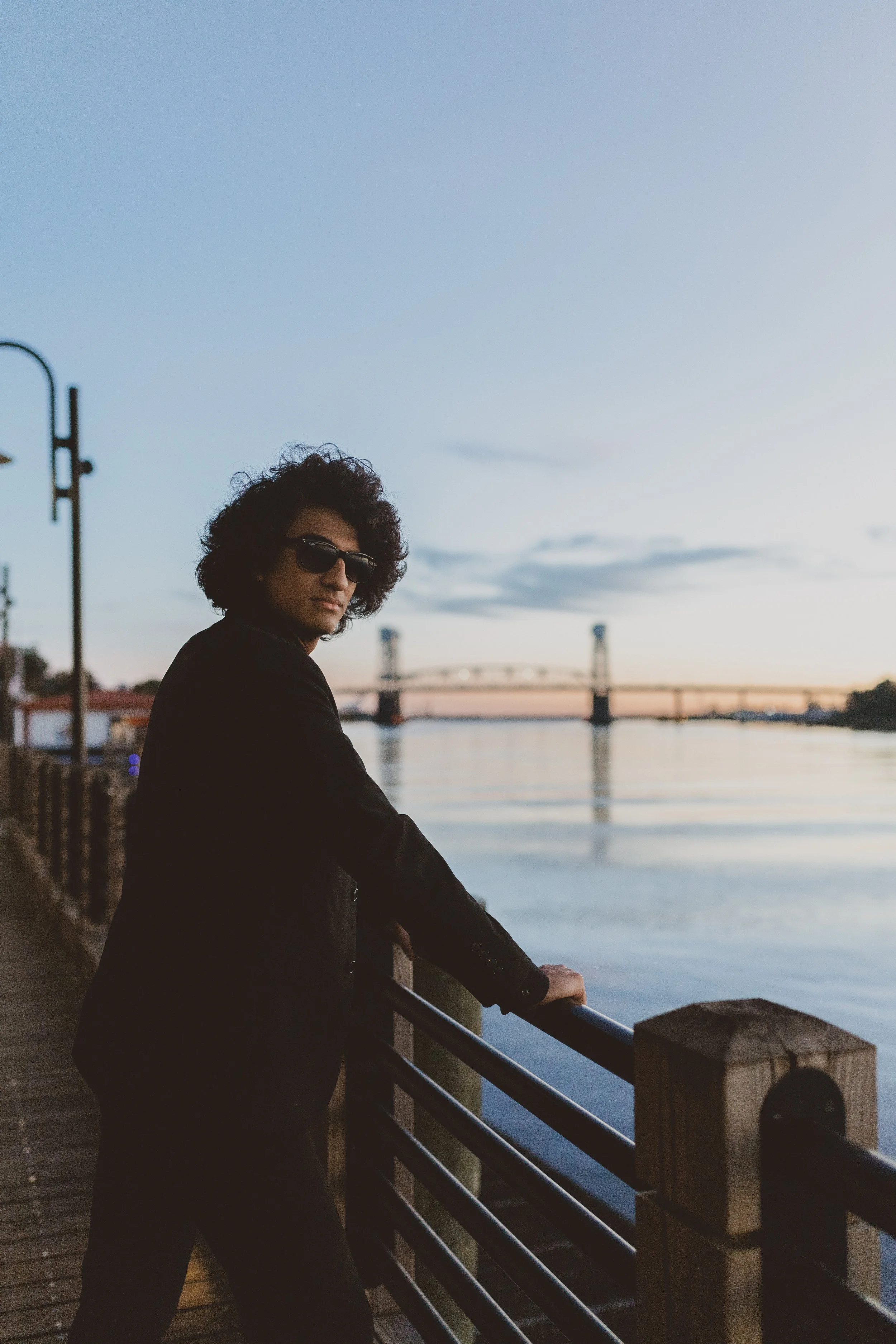 Person wearing sunglasses standing on a waterfront pier at sunset