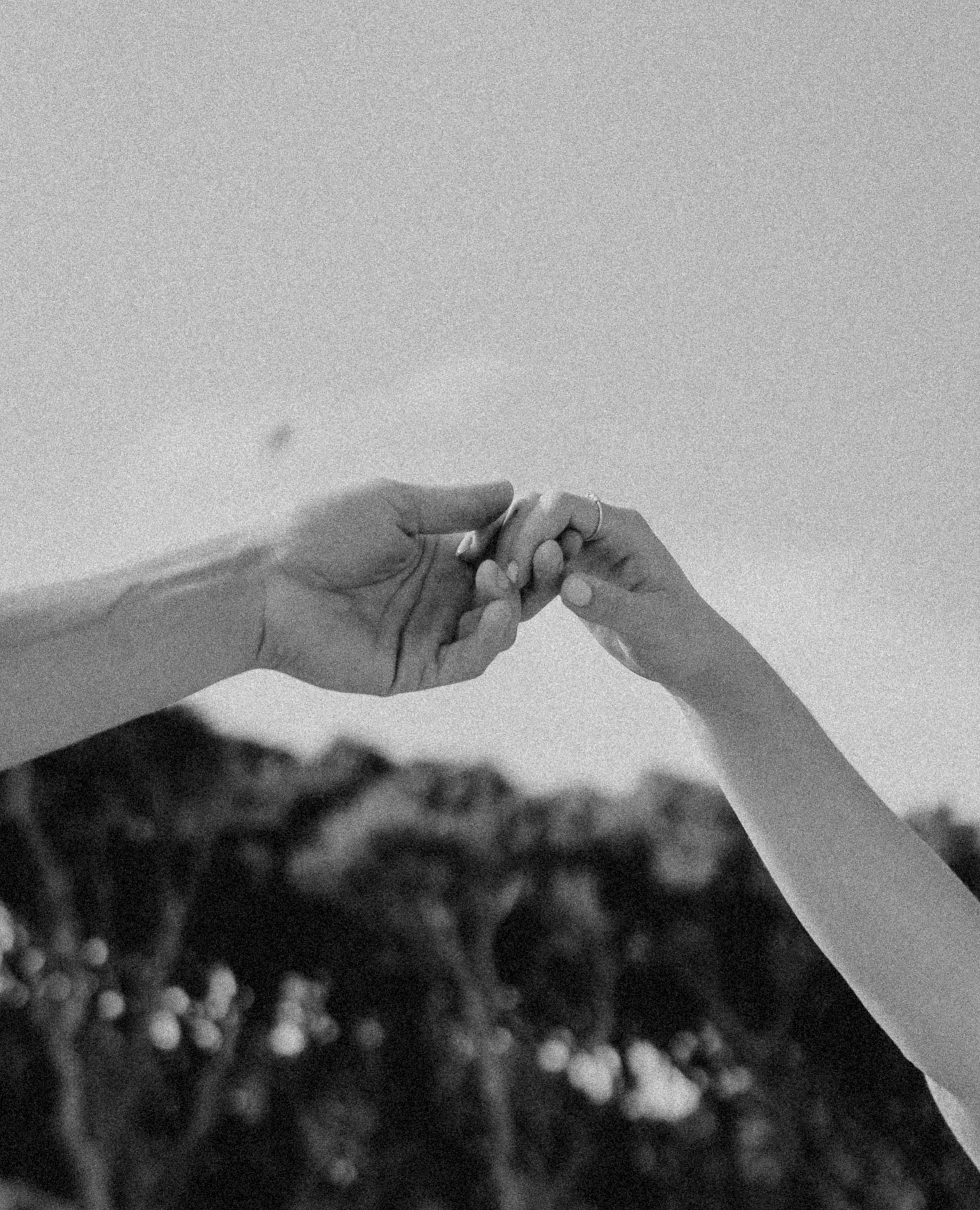 Close-up of two hands with light skin tone gently touching or holding each other against a grainy, dark background.