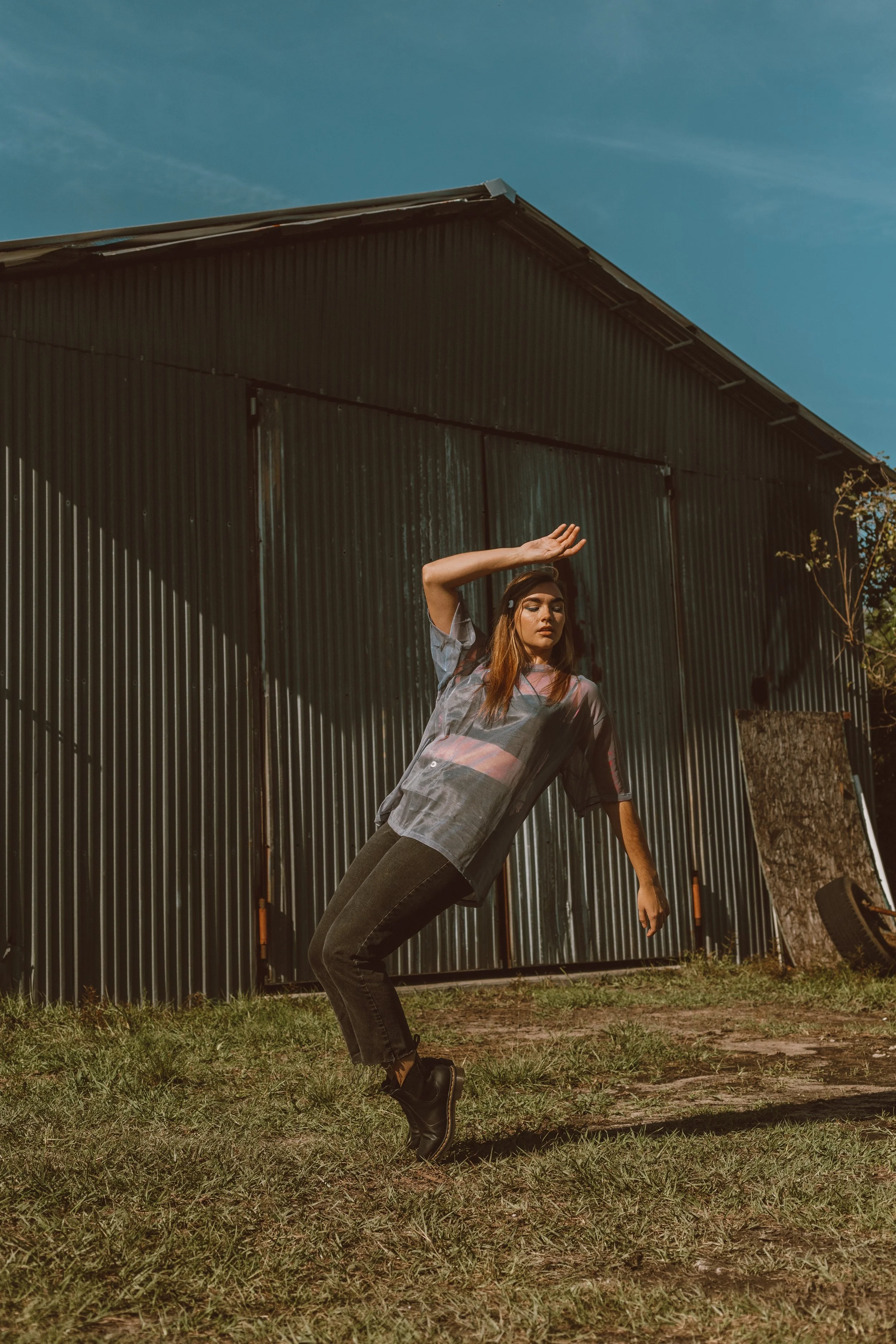 Woman posing outdoors in front of a corrugated metal barn under a blue sky