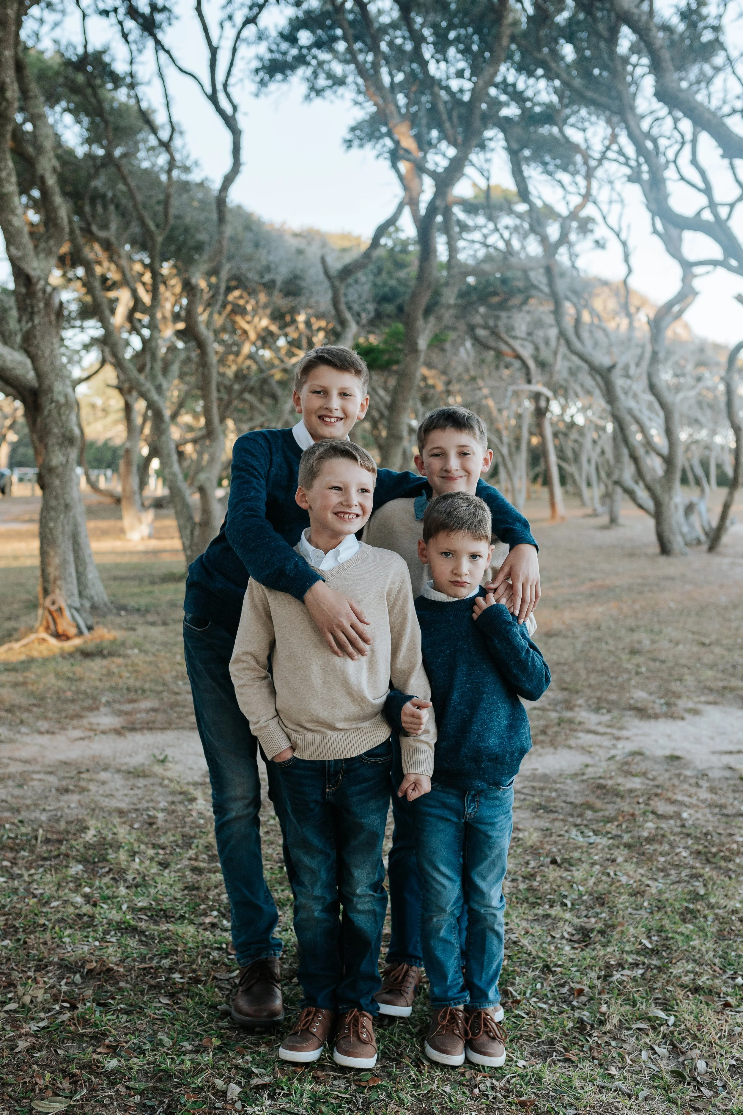 Four smiling boys posing together in a wooded park