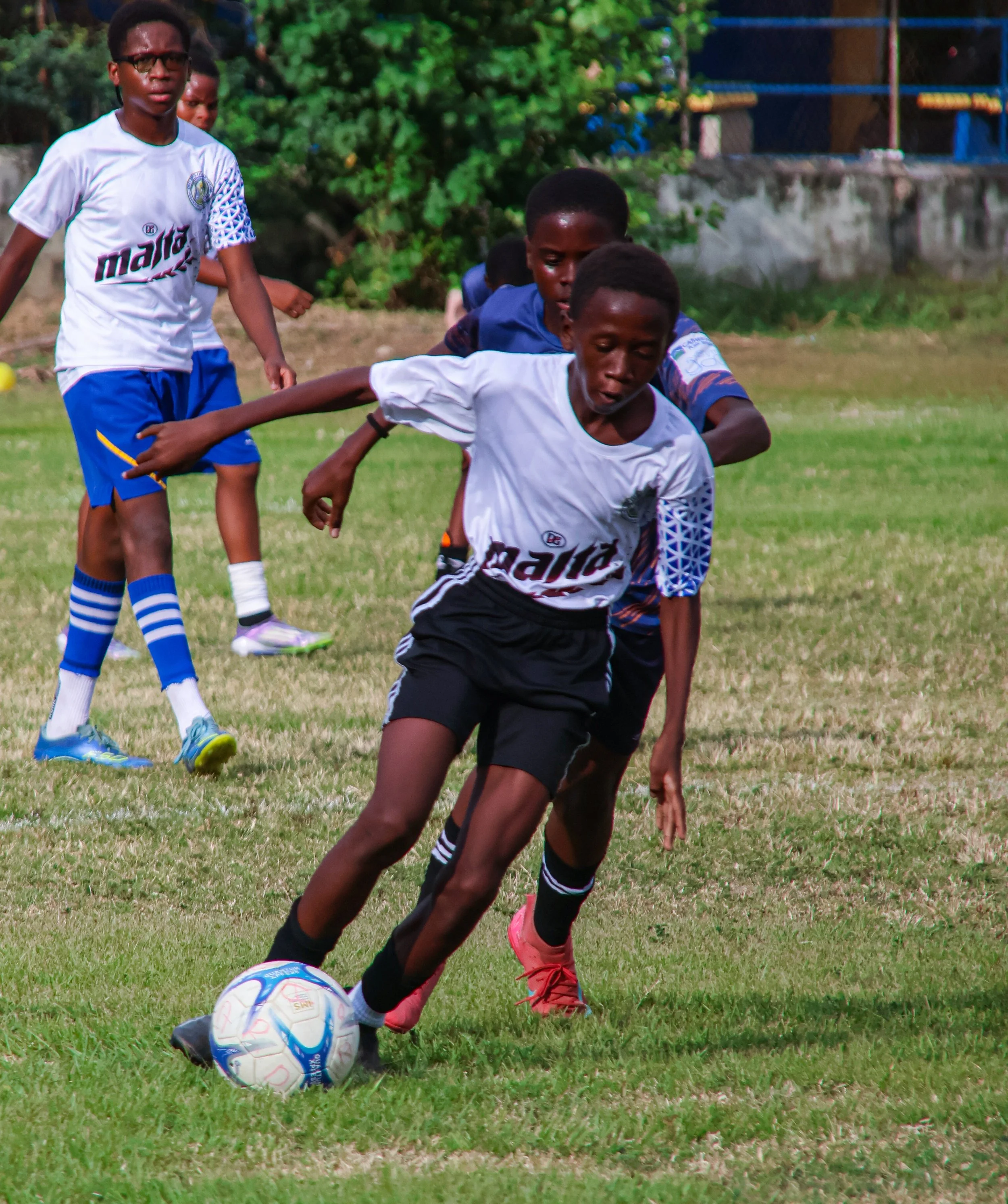 Young boys playing soccer outdoors on a grassy field, with one boy in a white and black uniform controlling the ball.