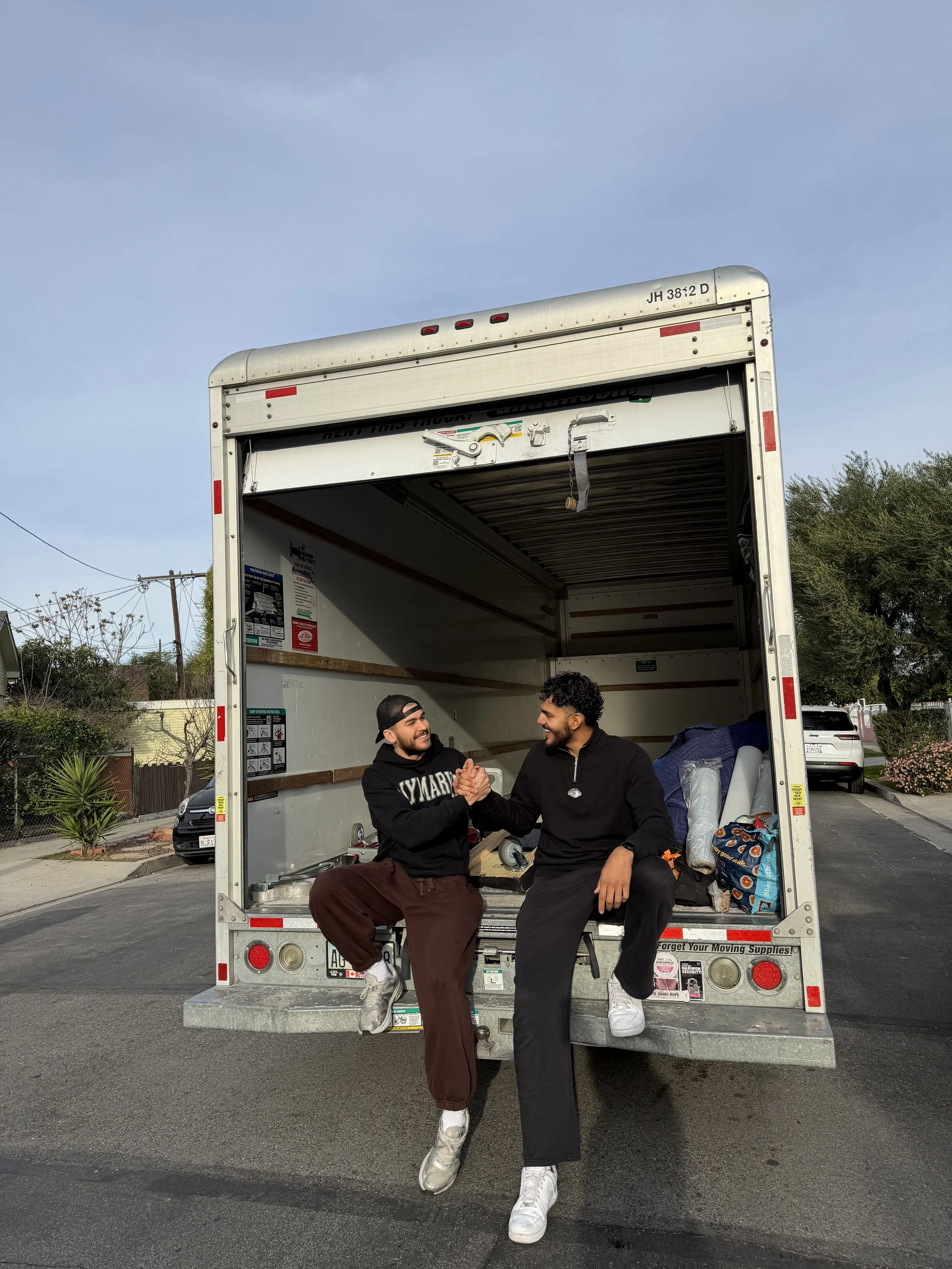 Two men shaking hands in the back of a moving truck in a residential neighborhood during the day.