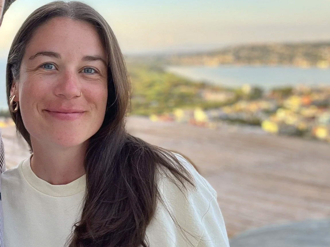 Smiling woman taking a selfie with a blurred river and cityscape in the background