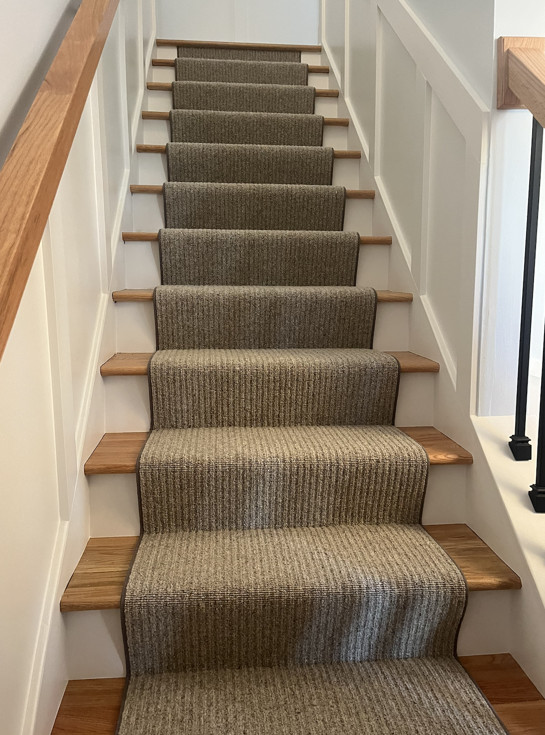 Carpeted stairs with wooden treads and white side panels in a home interior.
