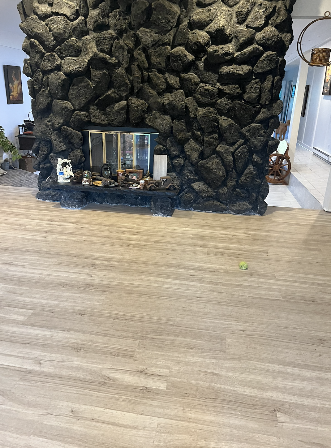 Living room with a large black stone fireplace, wooden flooring, a tennis ball on the floor, and various decorations on the fireplace mantel.