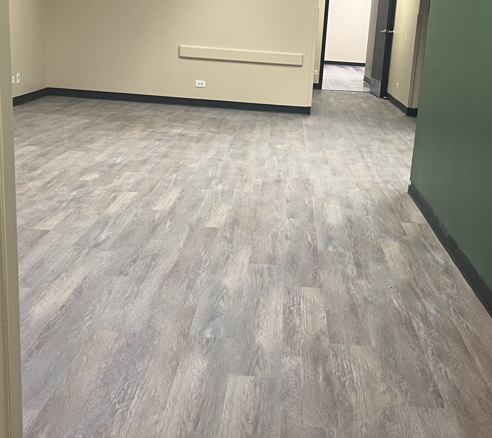 Empty room with greyish tile flooring, beige walls, and a doorway leading to another room.