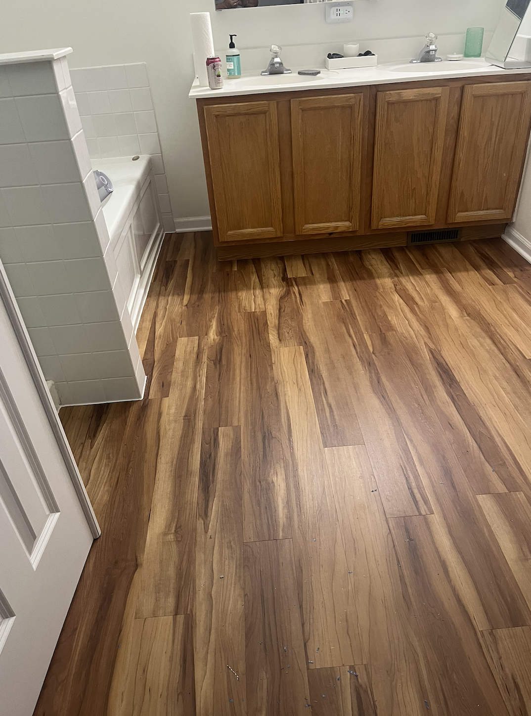 Bathroom with wooden floor, a white vanity with a mirror, and a small shower stall with white tiles on the left side.