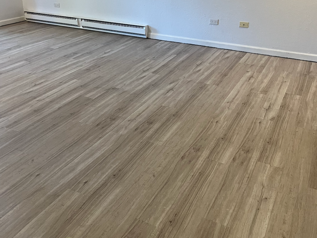 Empty room with light wood flooring, beige walls, electrical outlets, and baseboard heater.