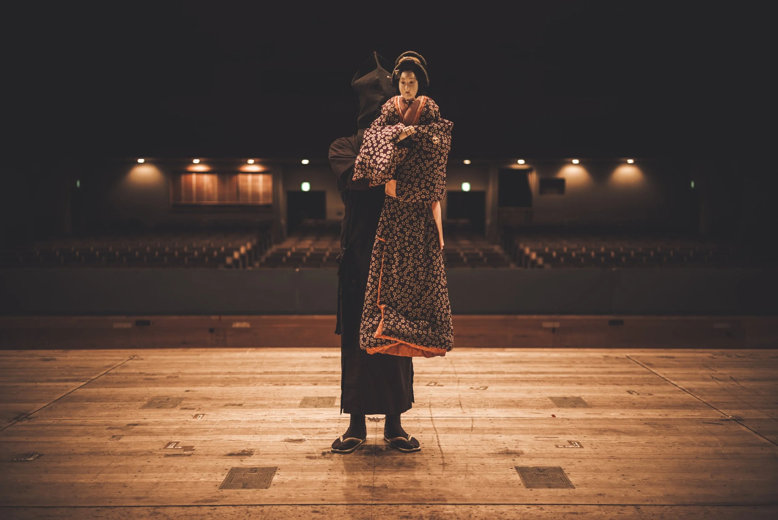 A person wearing traditional Japanese attire, standing on a stage in an empty theater with dim lighting.