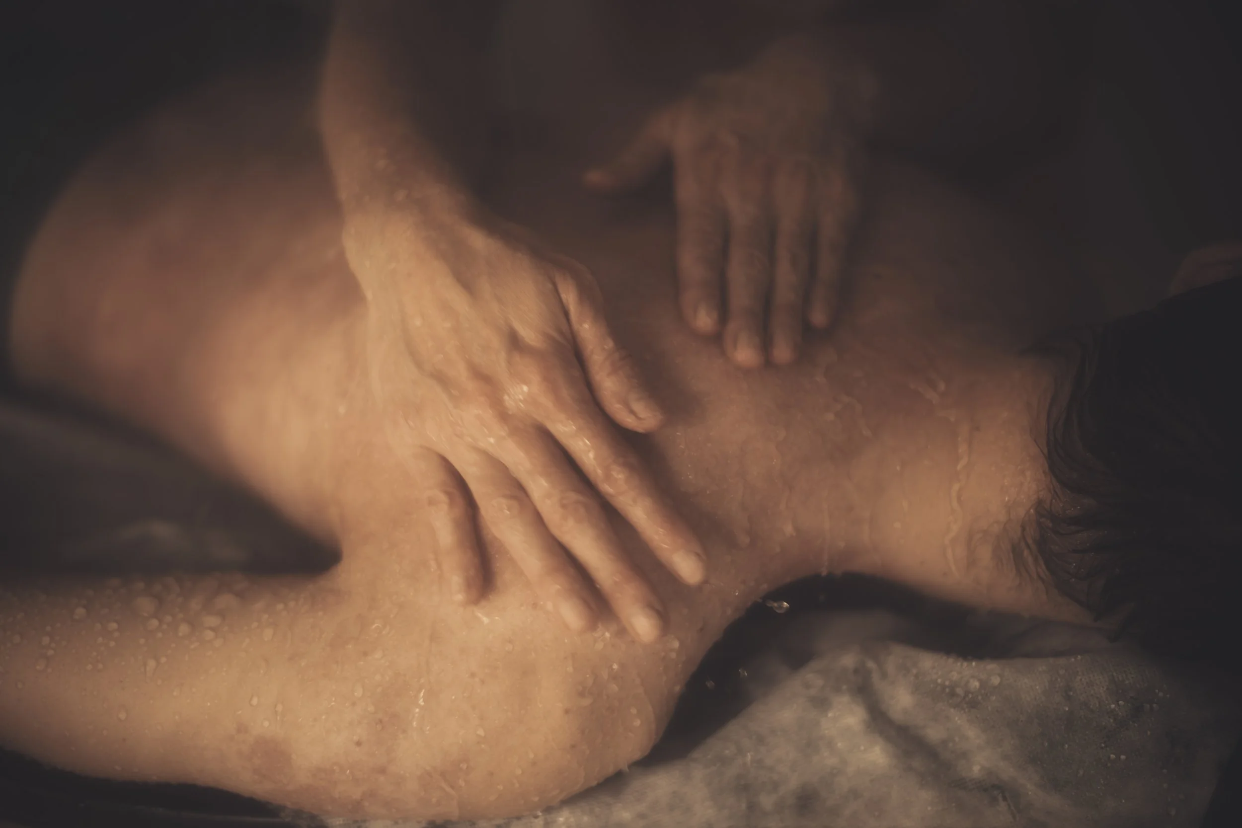 Person lying on a surface with hands resting on their stomach, in a dimly lit setting.