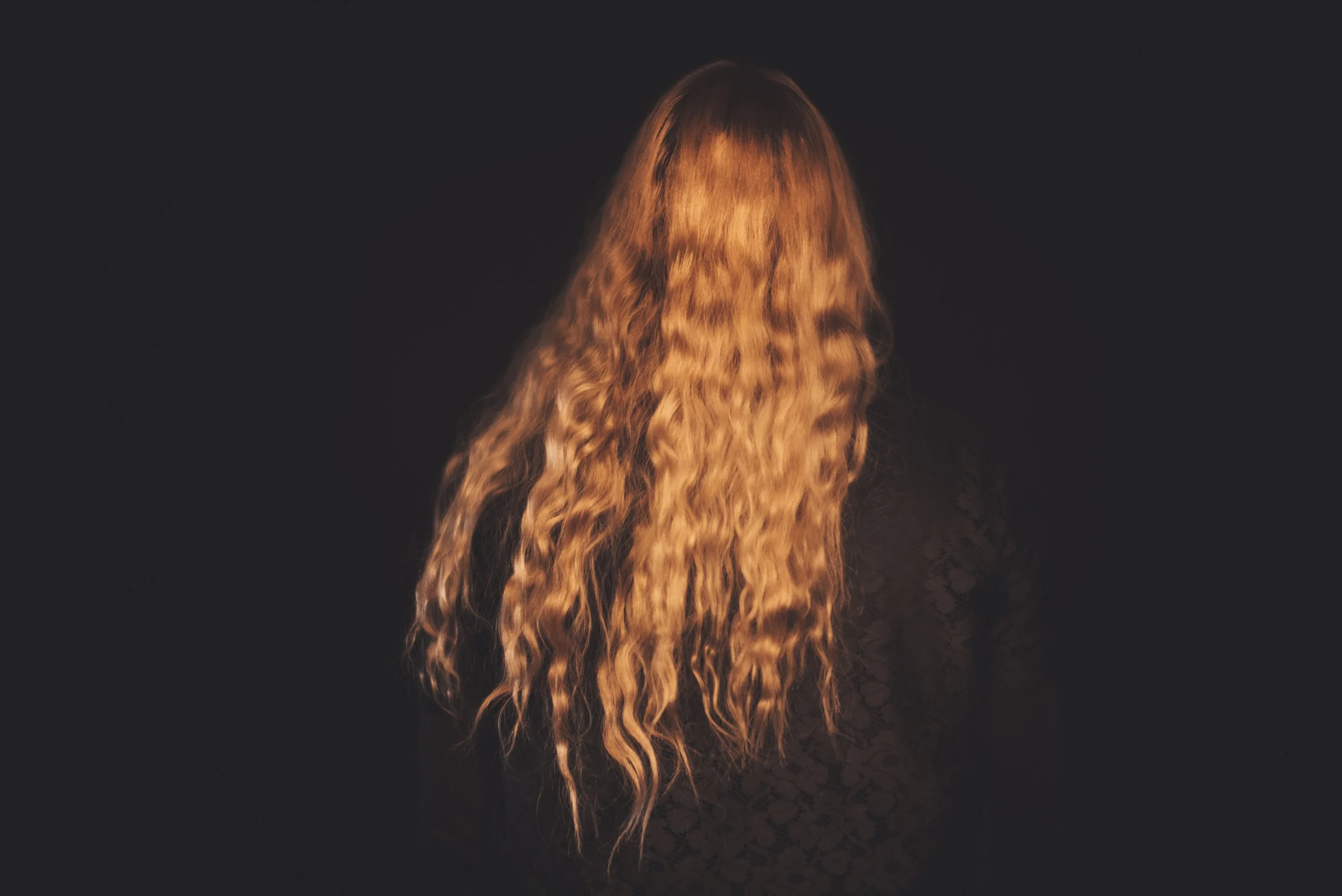 Long, wavy, reddish-brown hair against a dark background.