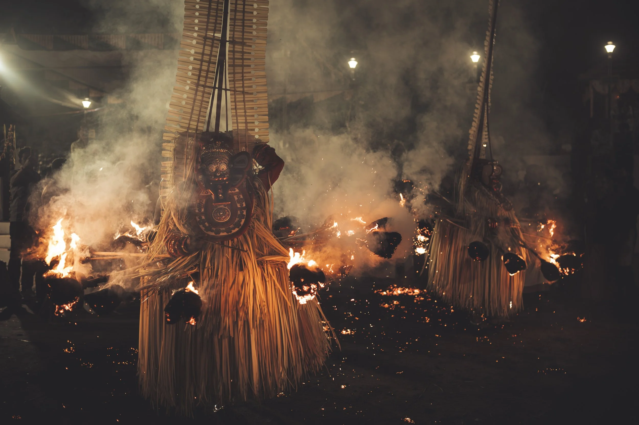 Traditional Balinese Barong dance performance with fire, featuring a large ornate lion mask and performers in costume, at night with fire and smoke.