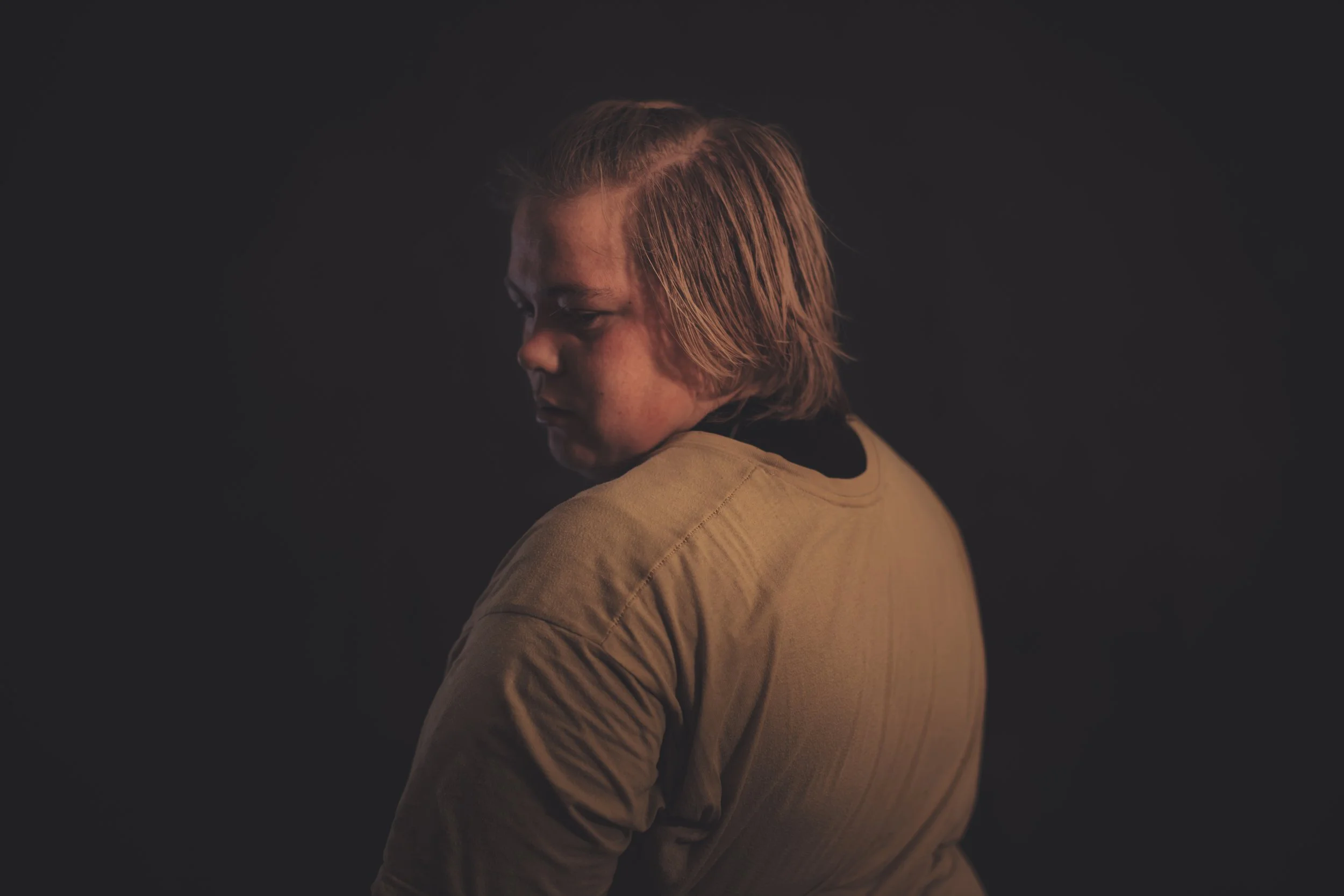 A person with medium-length reddish hair looking downward against a dark background.