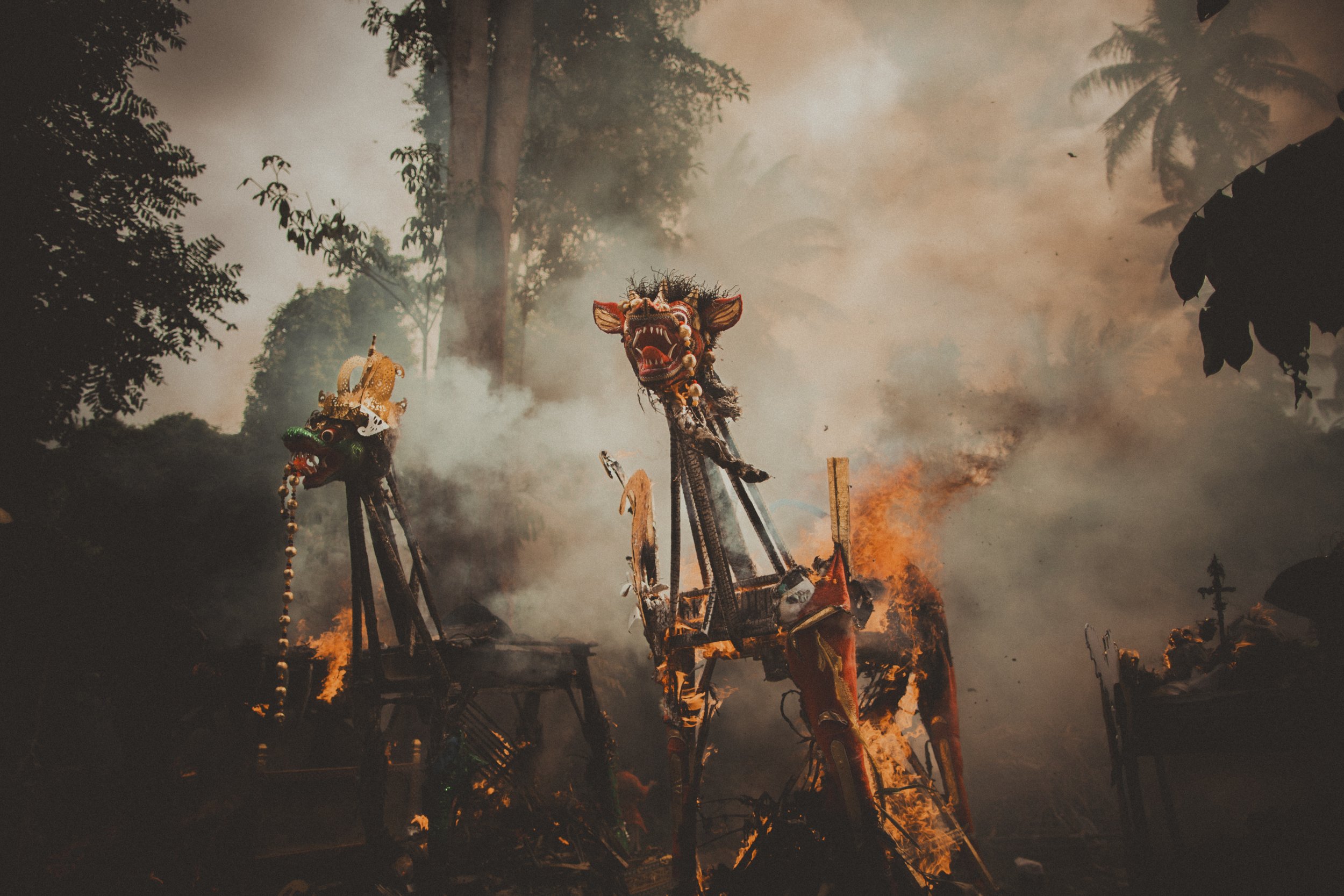 The image shows a scene of a fire with smoke and flames in a forest, including top of a structure with decorative dragon heads on poles.
