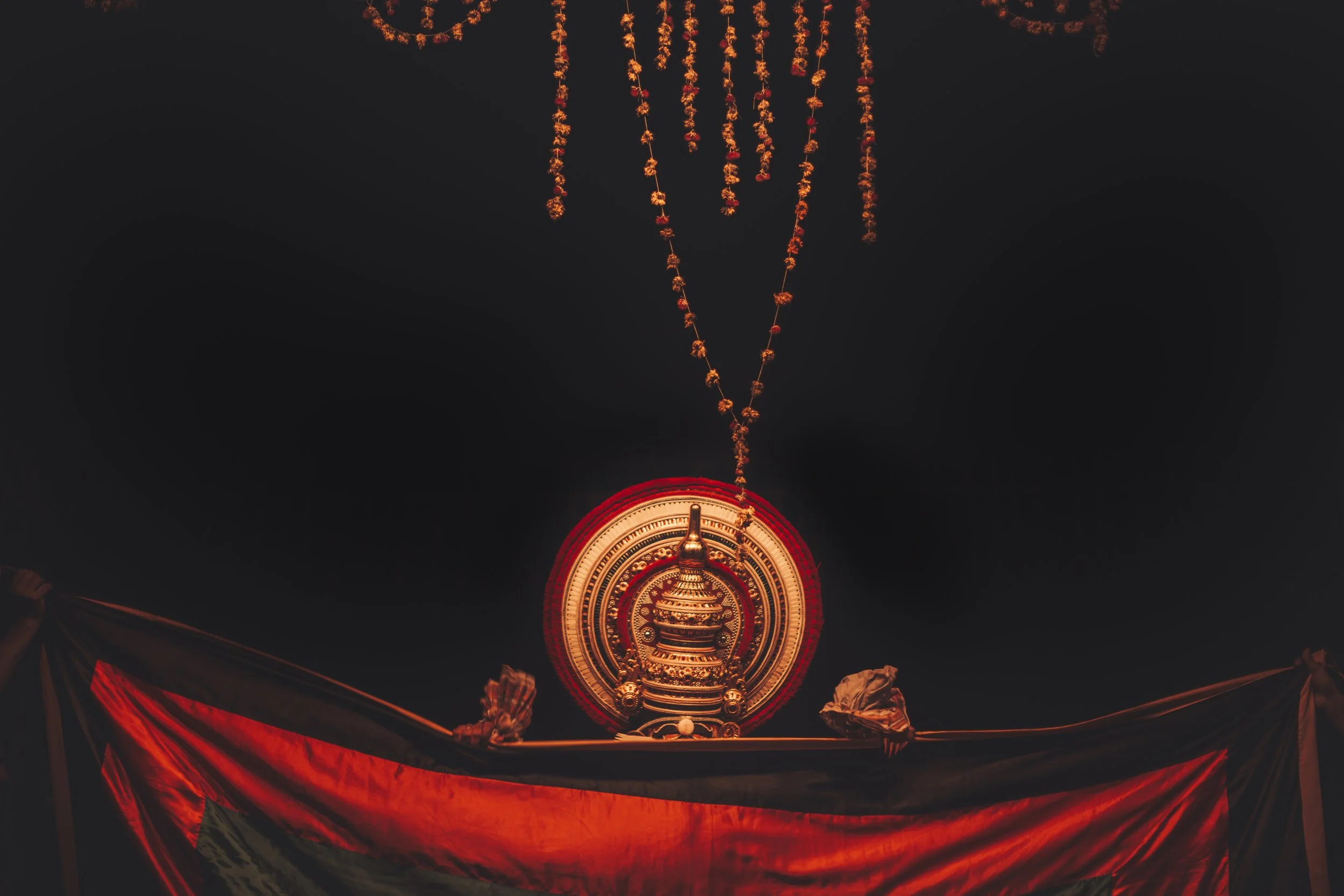 A brightly lit ornate temple or shrine with hanging orange decorations, dark background, and red drapery at the bottom.