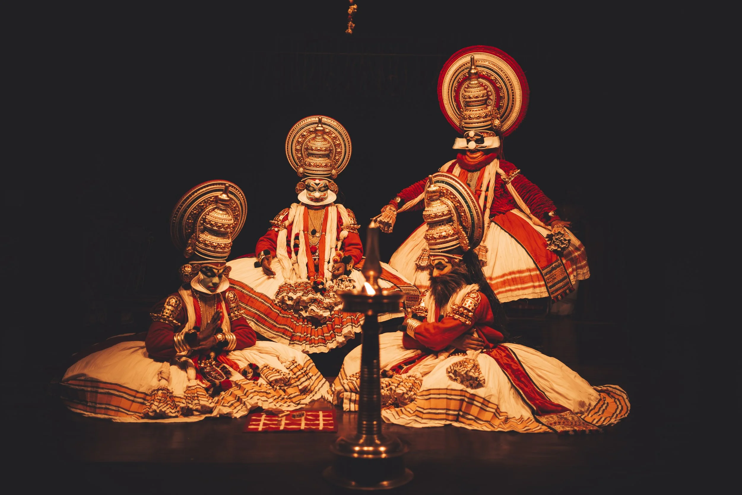 Traditional dancers in ornate costumes performing on stage, illuminated by a single candle in the foreground.