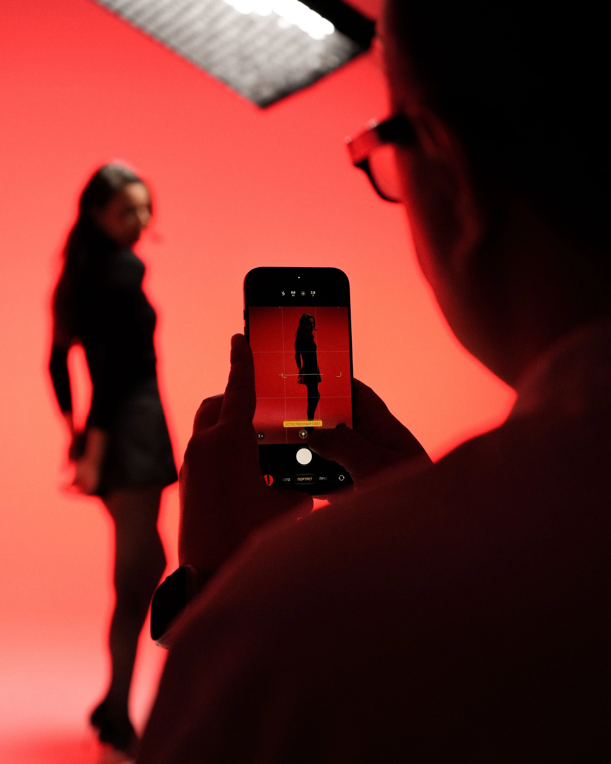Person photographing a silhouetted woman against a red-lit background with a smartphone