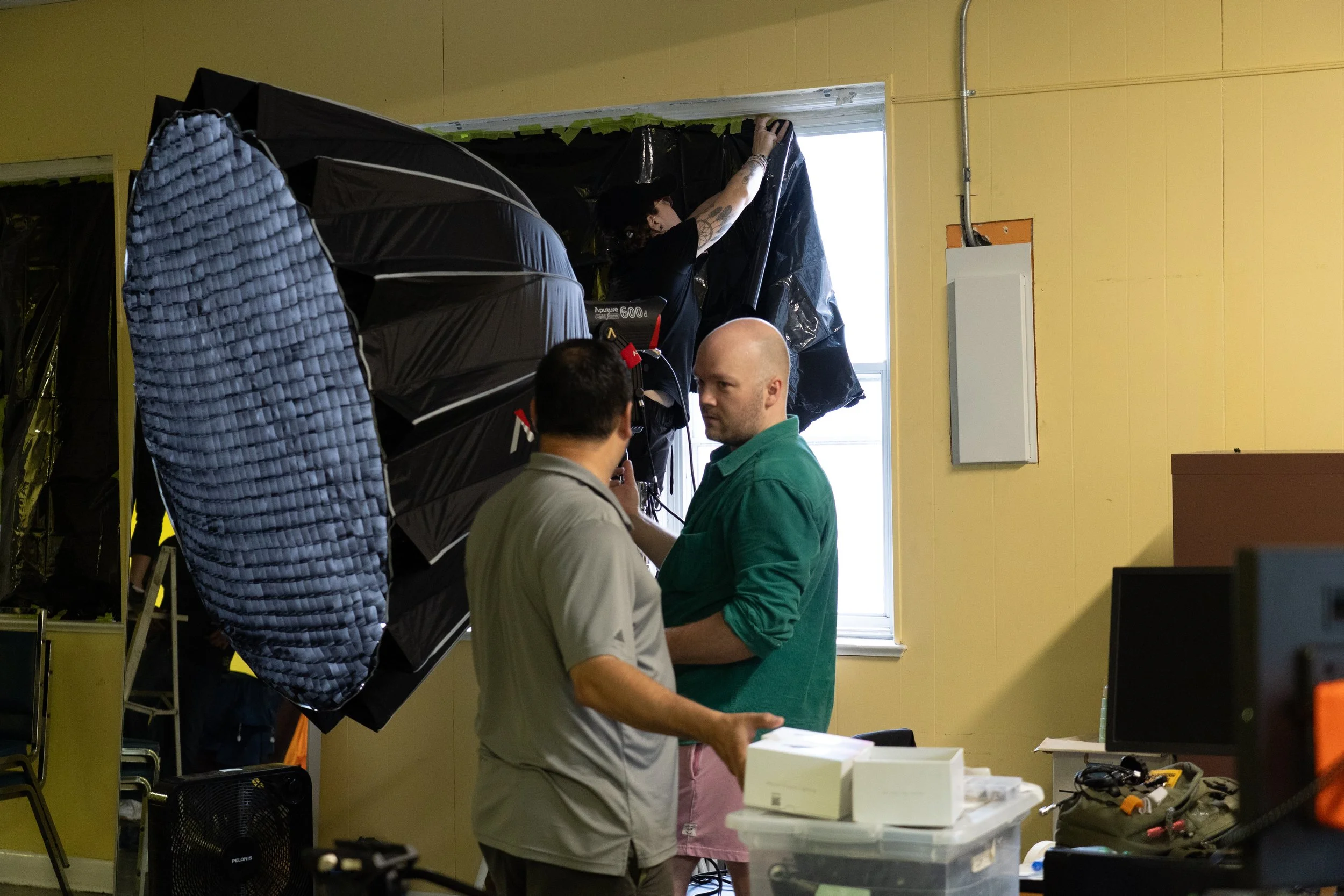 Film crew setting up black backdrops, lighting equipment, and reflective panels inside a room.