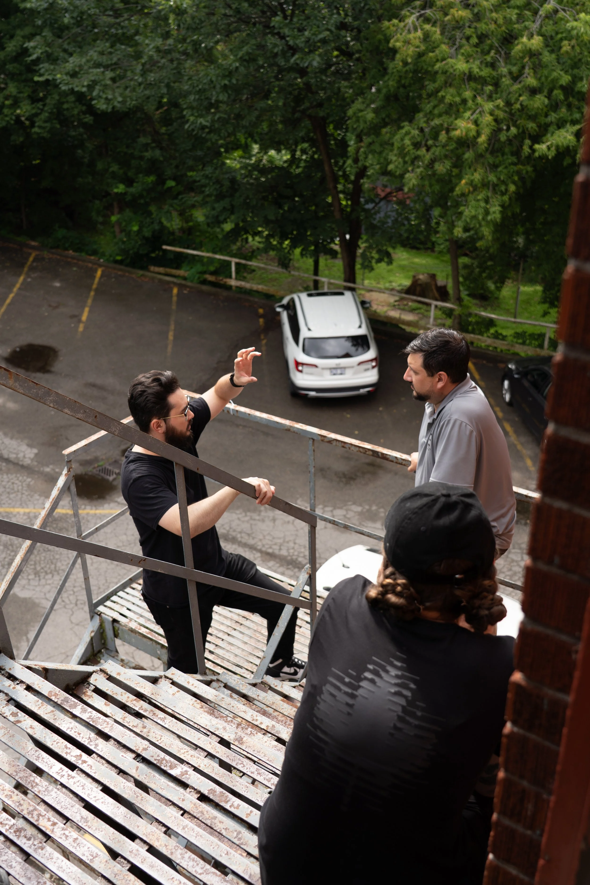 People standing on a weathered metal platform overlooking a tree-lined parking lot with a white car.