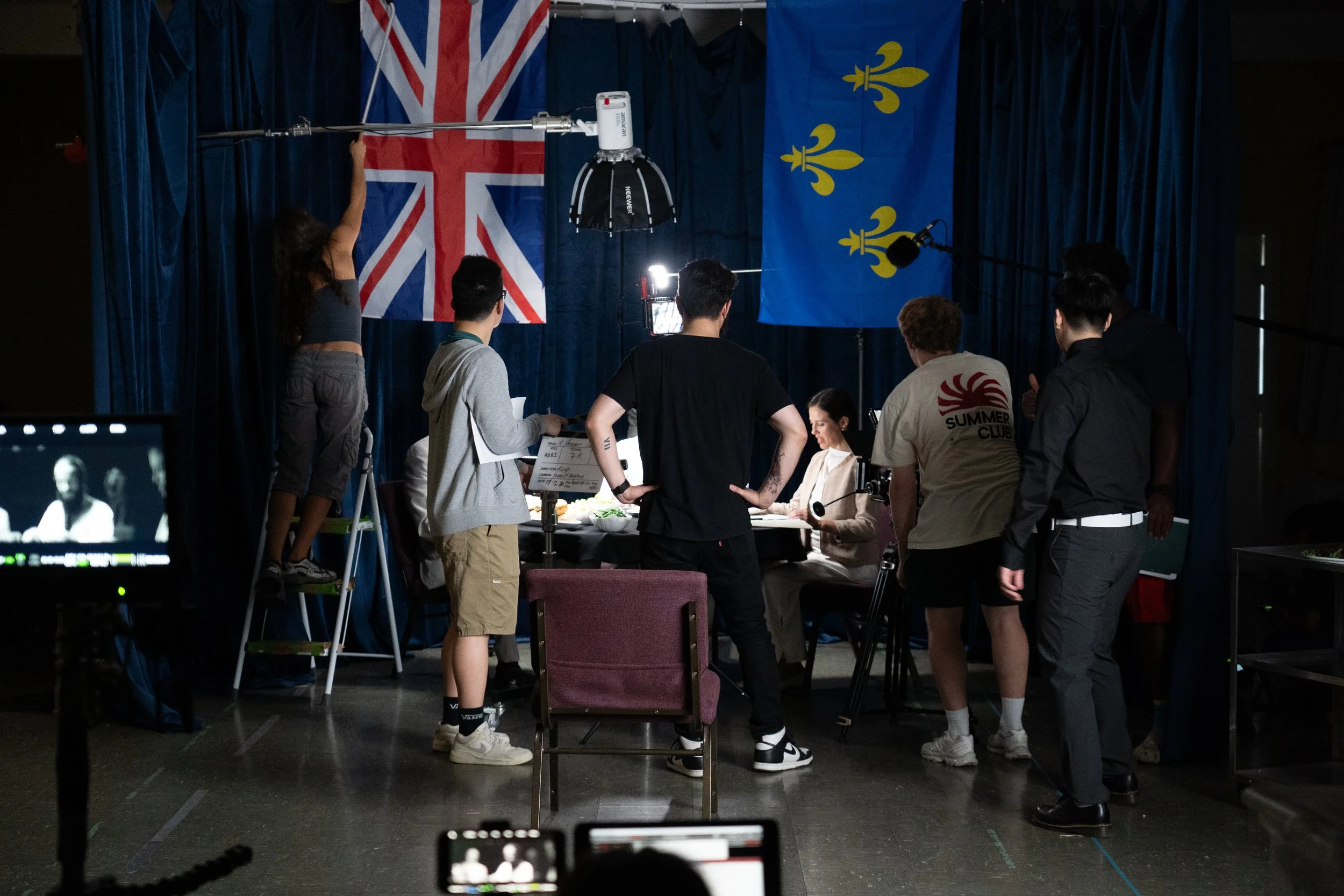 Film crew shooting a scene on a set with Union Jack and blue fleur-de-lis flags