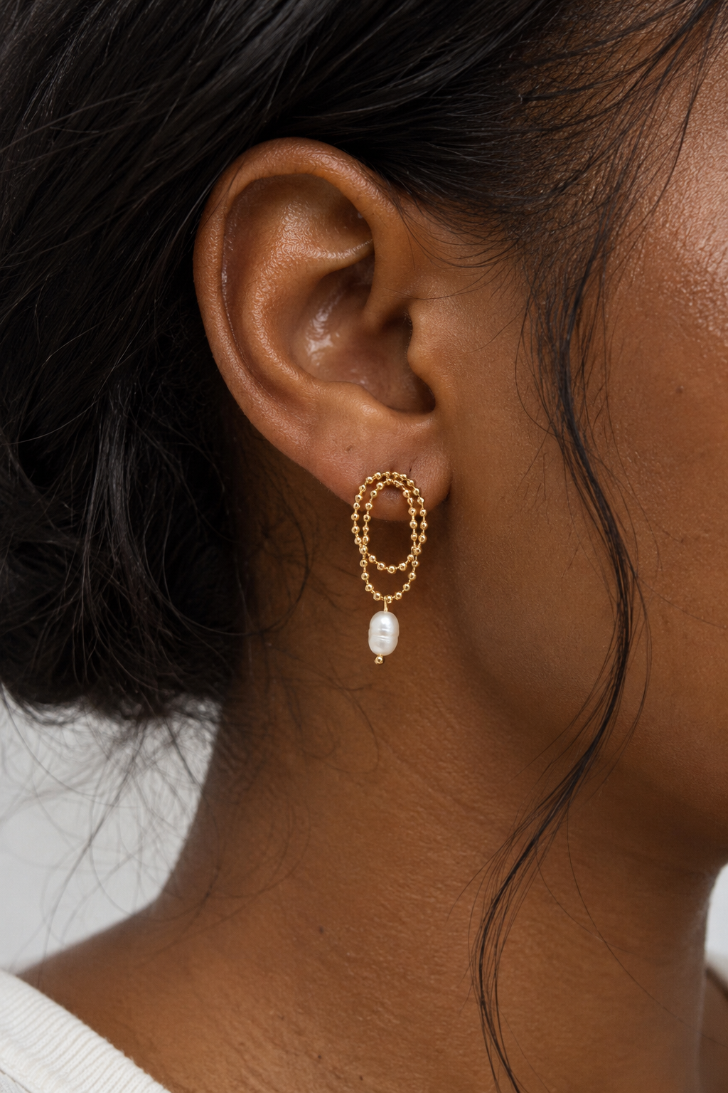 Close-up of a gold drop earring with a pearl pendant on a woman's ear