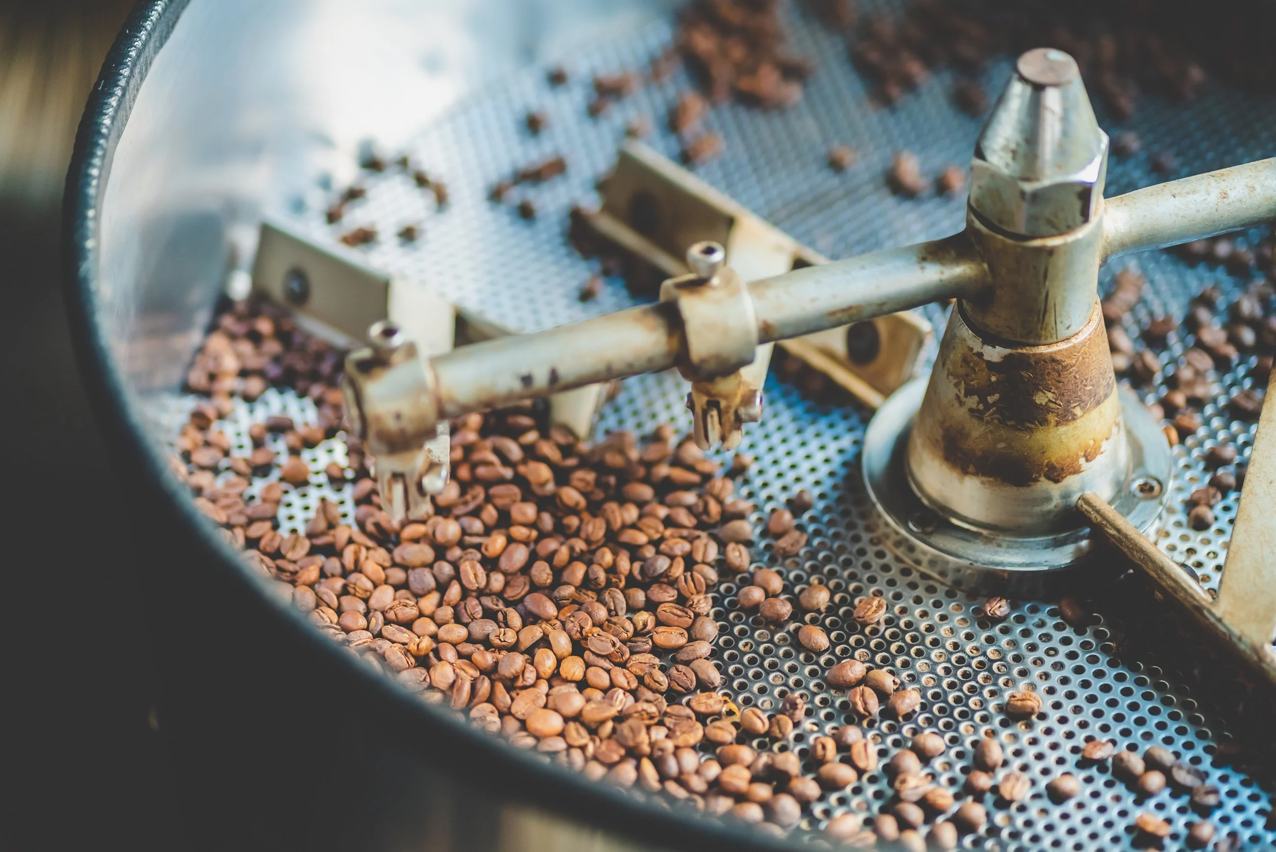Coffee beans on a metal roasting machine with a rusty, vintage appearance.