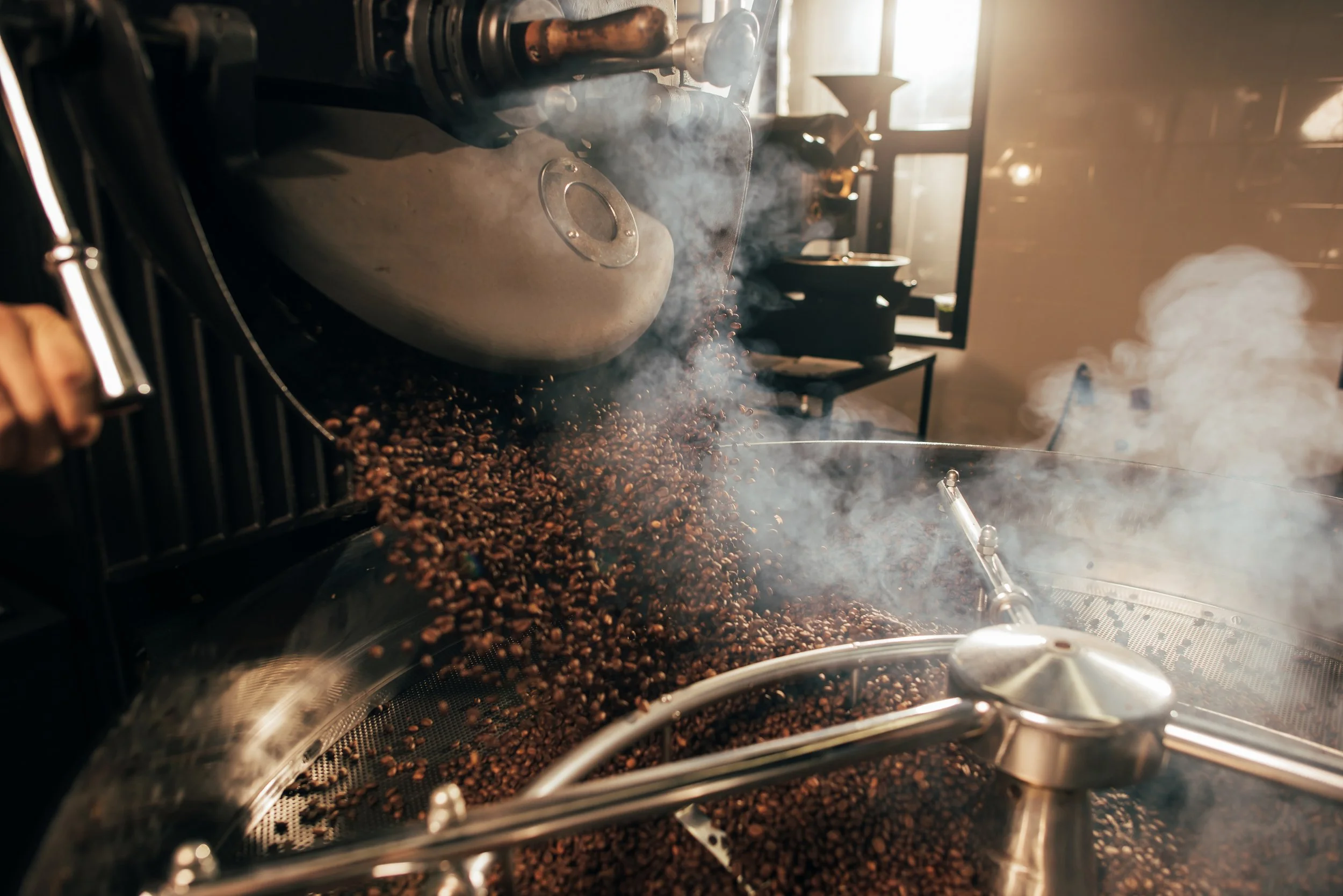 Coffee beans being roasted in a machine with steam or smoke rising.