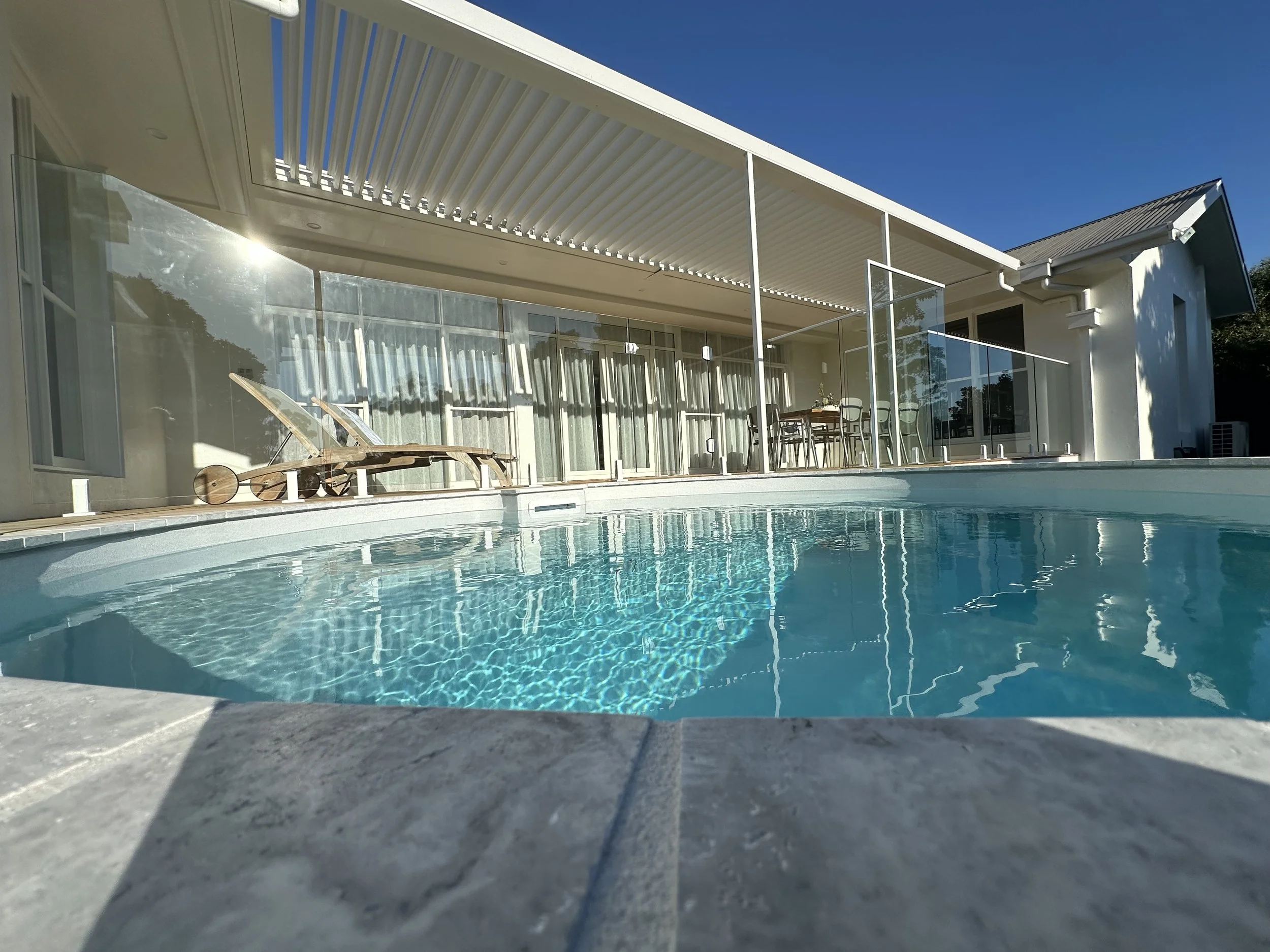 View of a modern house with a swimming pool and outdoor dining area under a clear blue sky.