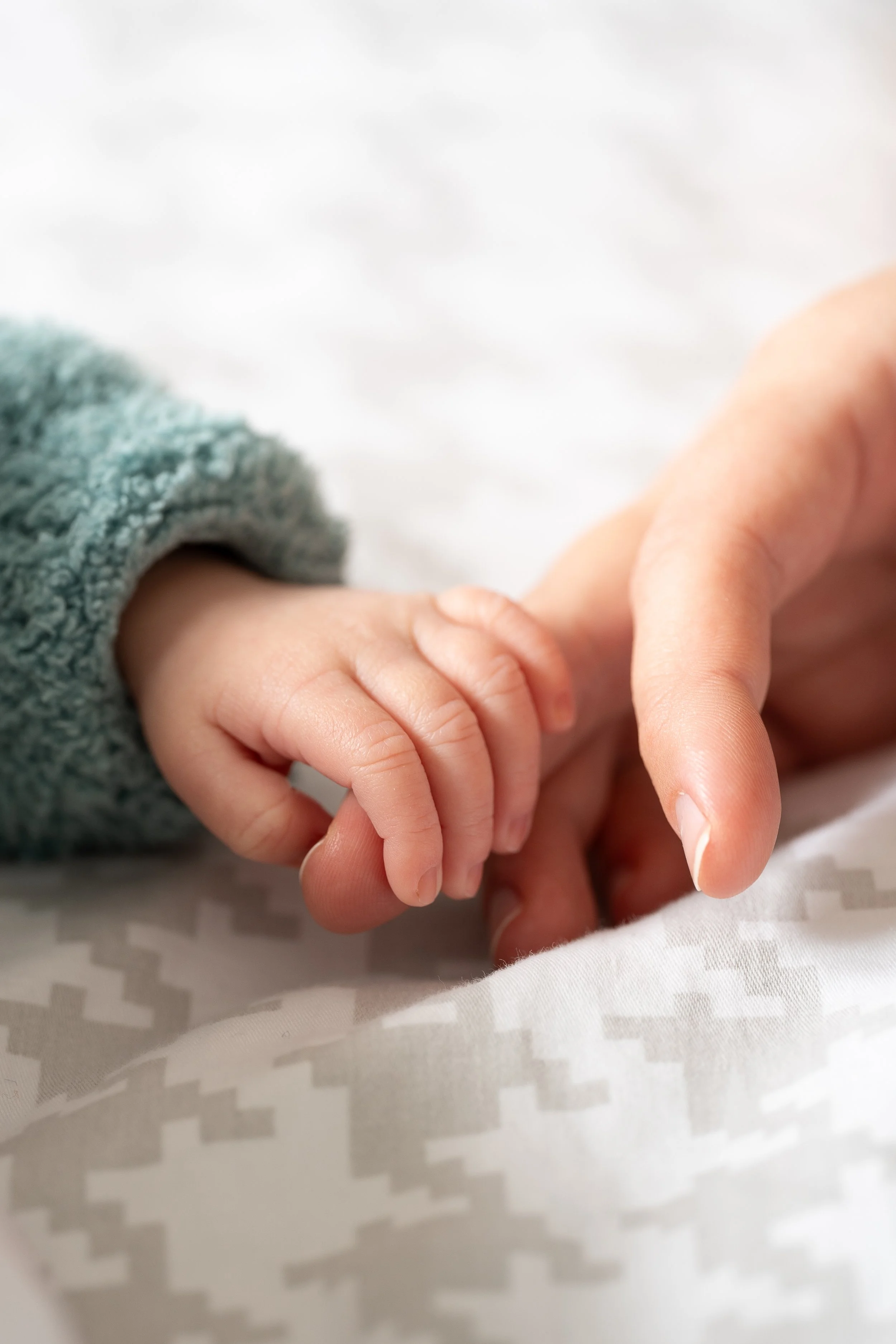 Un adulte et un bébé se tiennent par la main, le bébé porte un vêtement en molleton gris et l'adulte un vêtement blanc.