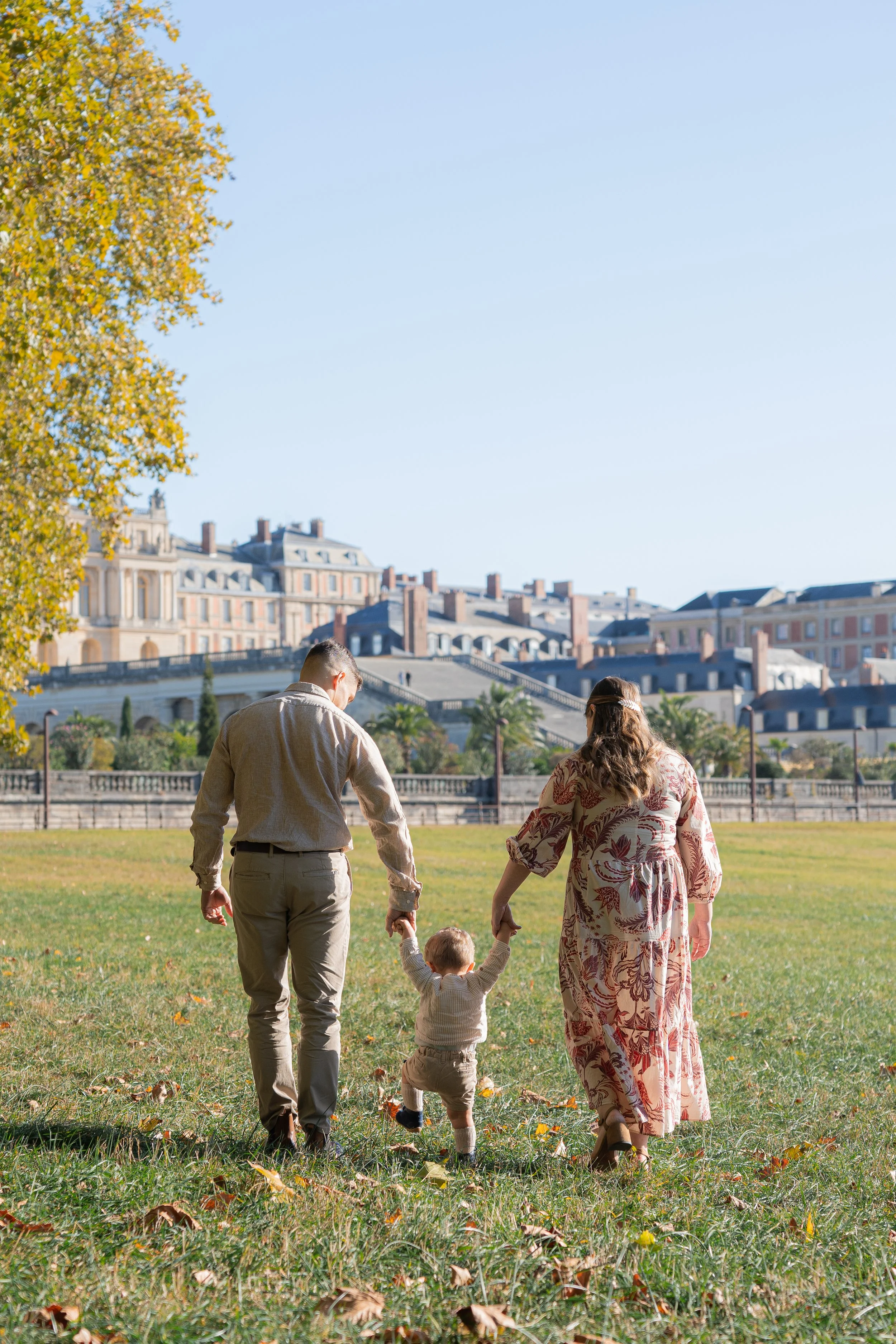 Famille marchant dans un parc en automne, avec des maisons anciennes en arrière-plan.
