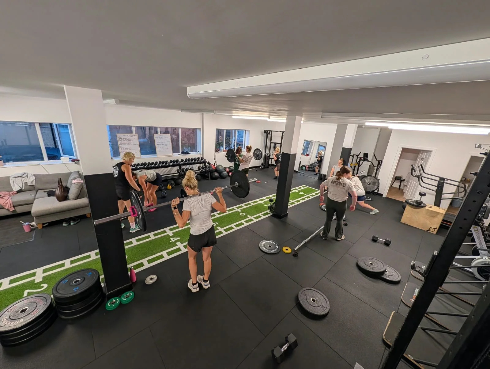 People working out in a gym with weights, barbells, and fitness equipment, including a treadmill, lifting weights, and performing core exercises.