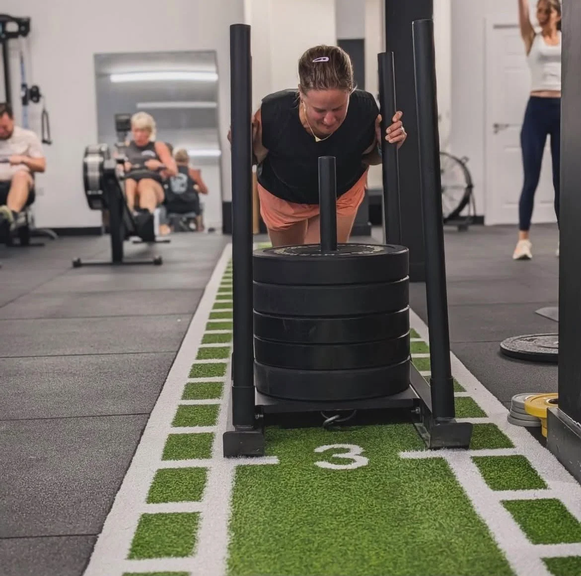 Woman pushing a weight sled at a gym during a workout.