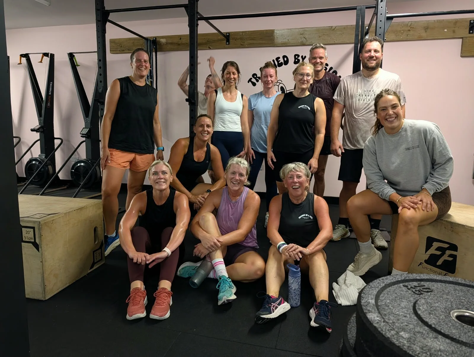 Group of people at a gym, posing for a photo, some sitting and some standing, with workout equipment in the background.